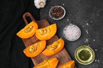 Orange pumpkin slices on wooden board with salt pepper and oil