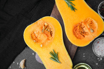Butternut squash halved with rosemary and spices on dark background, natural ingredients for...