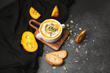Pumpkin soup in a bowl with fresh bread and seeds on a dark background