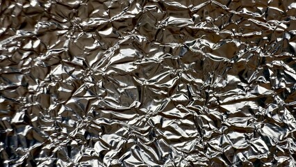 crumpled reflective silver foil surface with glossy metallic folds and shiny light reflections...