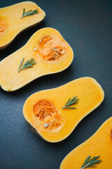 Halved butternut squash with rosemary sprigs on dark textured surface, top view