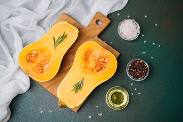 Butternut squash halved with rosemary seasoning and cooking oil on a wooden board with salt and...