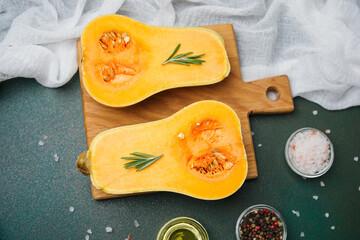 Butternut squash halves on cutting board with rosemary, salt, and peppercorns for cooking