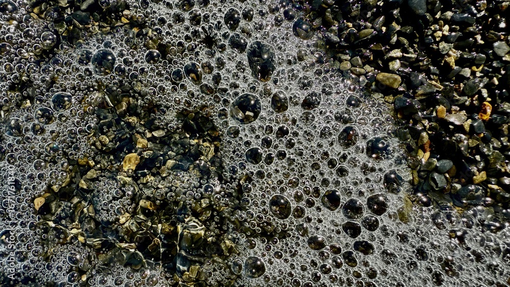 Poster shimmering seafoam bubbles on wet pebbles creating abstract coastal texture ideal for background or 