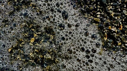 shimmering seafoam bubbles on wet pebbles creating abstract coastal texture ideal for background or natural pattern design