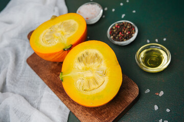 Halved orange pumpkin on cutting board with oil and spices, dark green background, close up