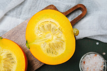 Vibrant yellow pumpkin cut in half on wooden board with salt grains and white fabric