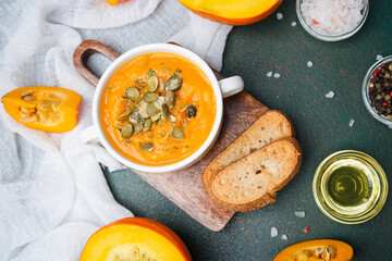 Warm pumpkin soup in bowl with seeds, bread, and oil, autumn healthy meal