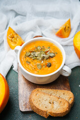 Bowl of pumpkin soup topped with seeds and herbs served with crusty bread slices on a wooden board.