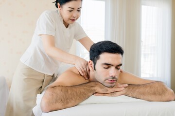 Asian female therapist giving relaxing shoulder massage to young man at spa, wellness, stress...