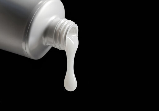 Creamy white substance oozes from a gray metal tube against a dark background in a creative setup