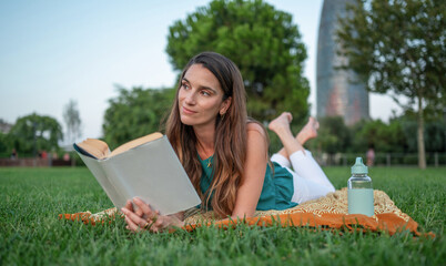 Young woman reading a book and relaxing in a park in barcelona