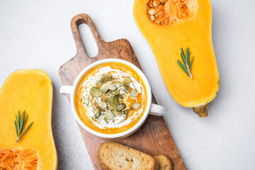 Butternut squash soup served with seeds and herbs on a wooden board with fresh squash slices