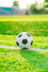 A soccer ball rests near the sideline on a lush green field as the sun sets creating a warm golden...