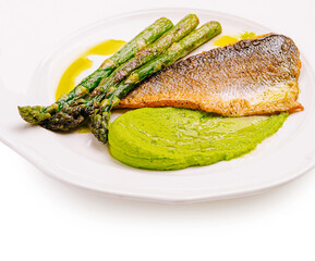 Grilled fish with asparagus and green pea puree served on a white plate