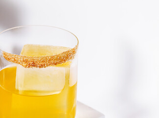 Bright yellow cocktail with sugar rim and ice sitting on a white surface