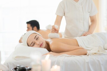 Obraz premium Couple receiving herbal compress massage in spa. A trending holistic therapy for stress relief, wellness, and self-investment.