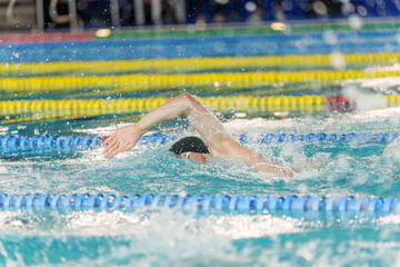 Athlete performing freestyle stroke during a swimming competition in indoor pool lanes