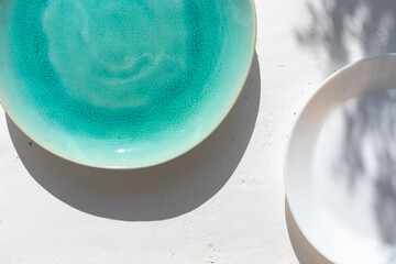 Empty turquoise ceramic plate on white plaster background with myrtle leaves shadows. Spring or summer table setting.