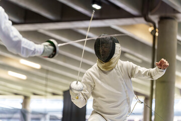 Two athletes in protective gear competing in a fencing match with epee swords