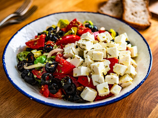 Greek style salad - fresh tomatoes with feta cheese and black olives on wooden table	