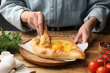 Woman eating delicious khachapuri at wooden table, closeup