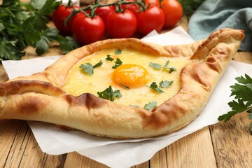 Tasty khachapuri with cheese, egg, tomatoes and parsley on wooden table, closeup