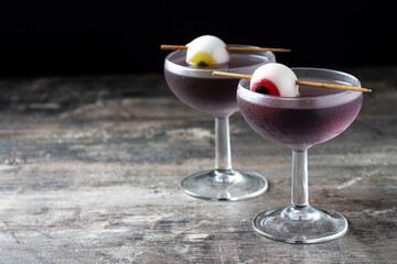 Purple Halloween cocktail garnished with candy eye on wooden table and dark background. Copy space