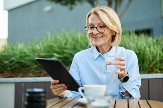 Portrait of a mid aged mature businesswoman using a laptop tablet and drinking coffee in a coffee shop