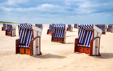 Blue and white striped beach chairs on sandy beach of the North Sea island of Norderney in Wadden Sea National Park invite to sunbathe. A wonderful summer day by the sea in a German dream destination 