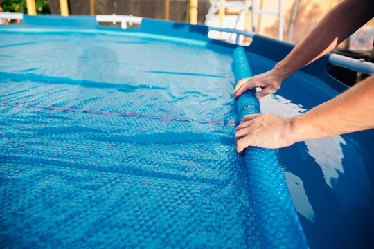 The blue pool cover is assembled into a roll by men's hands, the concept of summer recreation and pool maintenance.