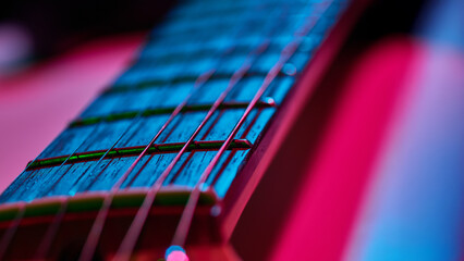 Guitar fretboard close up with neon blue and pink stage light reflections. Concept of retro music identity, creative covers, instrument advertising, and audio culture visuals.