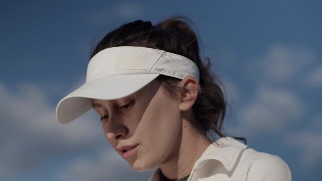 Woman golfer with visor hat focuses on ball shot against sky