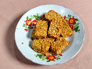 A pile of crispy fried tempeh that looks delicious and tasty, in a glass plate with a floral motif.