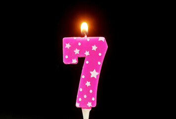 Burning pink with white stars birthday cake candle isolated on black background. Number 7.
