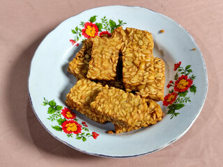 A pile of crispy fried tempeh that looks delicious and tasty, in a glass plate with a floral motif.