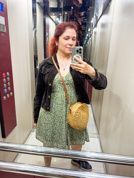Woman taking mirror selfie in elevator with smartphone. Everyday lifestyle, modern technology, and urban routine in personal perspective.