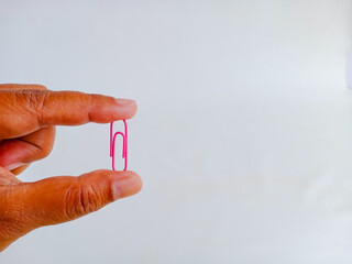 A hand holding a single pink paperclip on background, commonly used to organize or bind sheets of...
