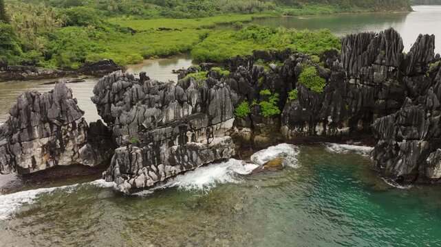 Aerial drone footage of Poule de Hiengh&egrave;ne black cliffs with lush greenery and waves breaking on reef in New Caledonia.