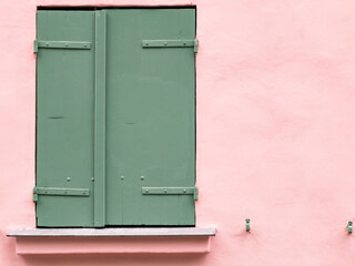 Closed green wooden shutters on a pink stucco wall. Minimalist architectural detail with pastel colors, vintage charm, and Mediterranean style