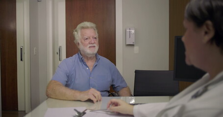 Obraz premium Senior man arriving for medical consultation, smiling and shaking hands with female doctor in clinic office while standing at desk during greeting