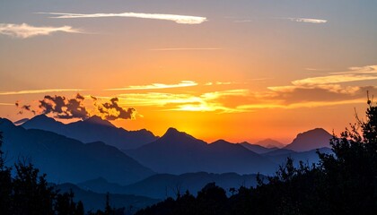 Obraz premium Stunning mountain range silhouette as the sun sets with vibrant orange hues painting the evening sky