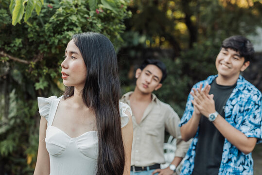 A composed young Asian woman looks away in silence as two smug young men behind her make inappropriate comments and catcall her outdoors.