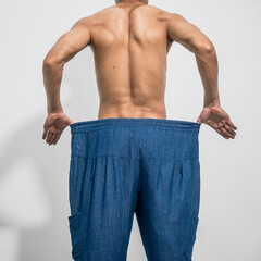 Closeup of slim Asian man wearing oversized jeans, reflecting his weight loss journey. Committed to...