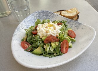 A delicious dish of tomato, avocado, stracciatella cheese and greens on a restaurant table