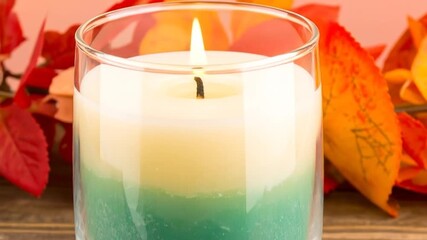 Glowing Candle with Teal Green and White Wax in Glass Vase on Wooden Table with Autumn Leaves Arrangement in Soft Light - Powered by Adobe