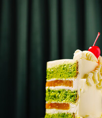 Delicious green cake with layers and cherry topping on dark background