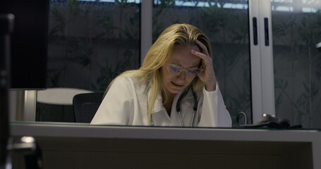Female doctor lowering head in despair showing signs of severe burnout during nighttime inside...