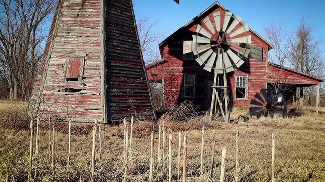 Old windmill and red barn in rural landscape under a blue sky