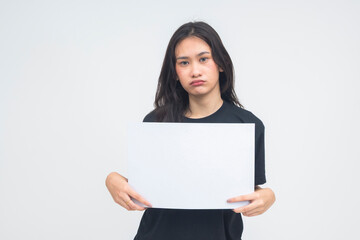 Naklejka premium A sad young Asian woman in a half body shot holding a white blank canvas while pouting, showing a disappointed and sorrowful expression. Isolated on a white background.